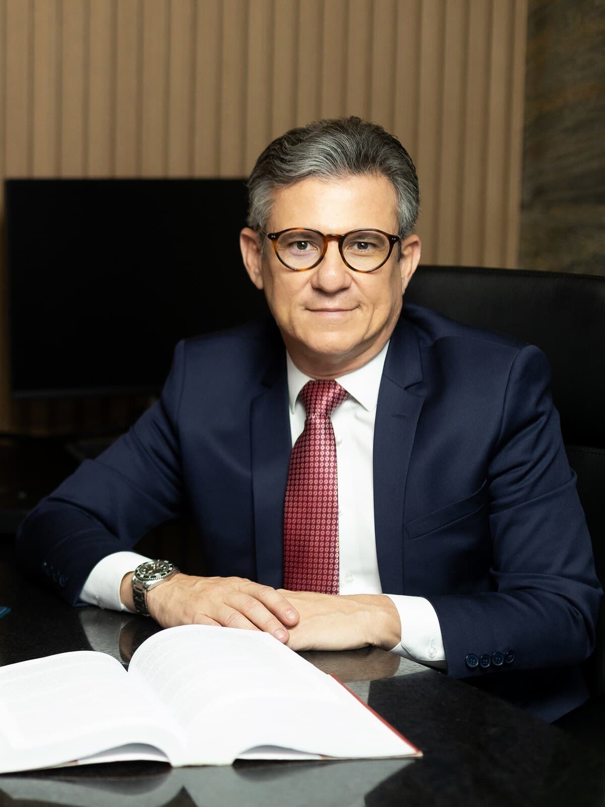 Dalton Medeiros Buarque, sócio fundador, à mesa de reunião do escritório, com um livro de legislação aberto à frente.