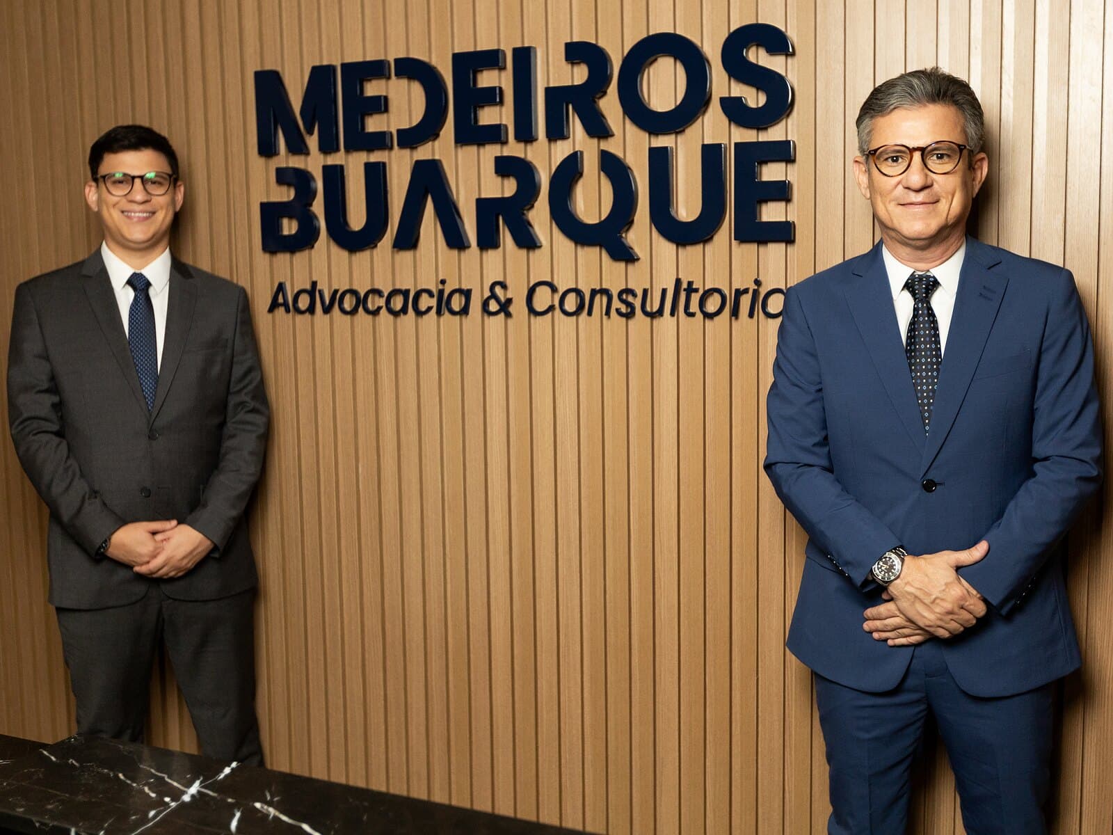 Caio Lucas Buarque e Dalton Medeiros Buarque, sócios do escritório, na recepção da sede, diante do letreiro Medeiros Buarque Advocacia & Consultoria.